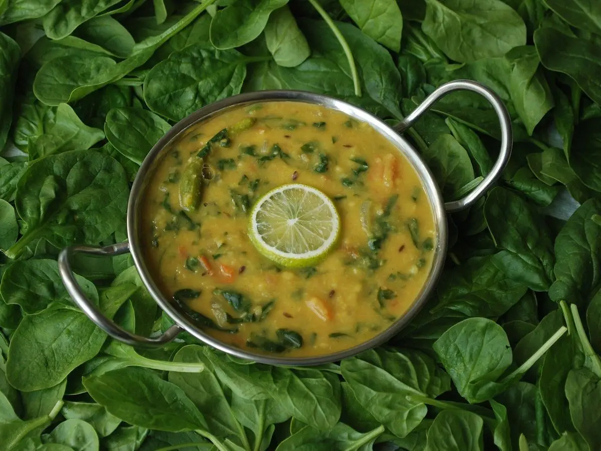 Cazuela de curry de lentejas con espinacas y una rodaja de lima sobre hojas de espinaca