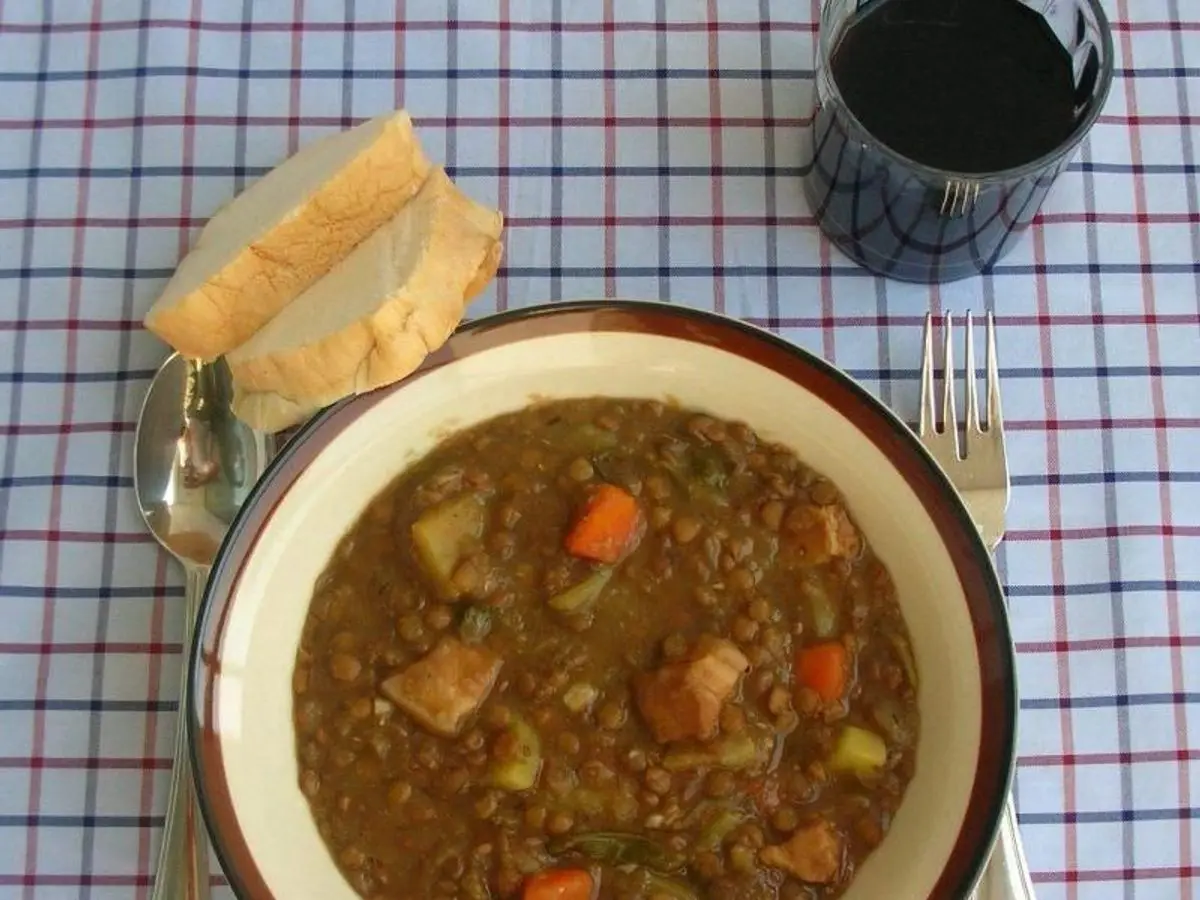 Plato hondo de lentejas guisadas con zanahoria y patata sobre un mantel de cuadros, con pan al lado