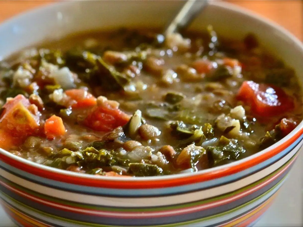 Cuenco a rayas de guiso de lentejas con verduras, tomate troceado y hojas verdes