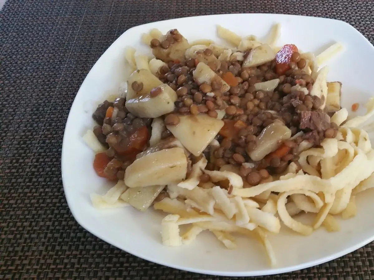 Plato blanco de lentejas guisadas con tacos de champiñón y pasta casera sobre un mantel gris