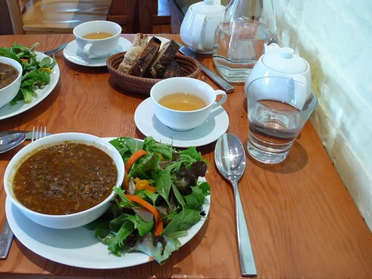 Cuenco de sopa espesa de lentejas con ensalada verde, pan y té sobre una mesa de madera