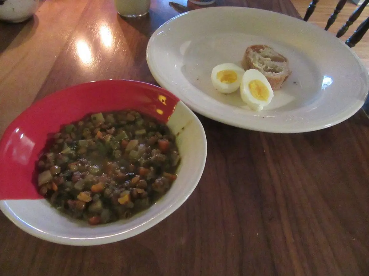 Cuenco rojo de lentejas guisadas con huevos duros partidos en un plato al lado