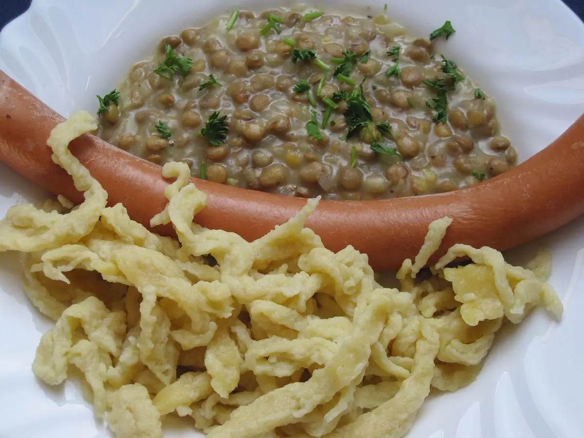 Lentejas con spätzle caseros y salchichas en un plato blanco