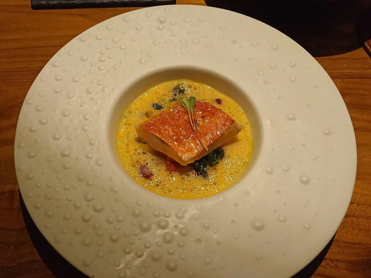 Filete de pescado a la plancha sobre salsa amarilla en un plato hondo blanco