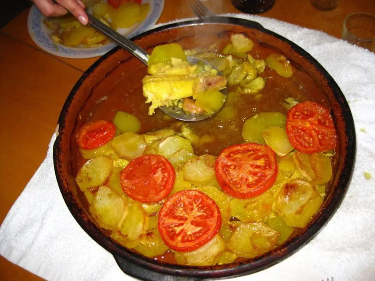 Cazuela de barro con patatas en rodajas, tomate y pescado guisados en su caldo