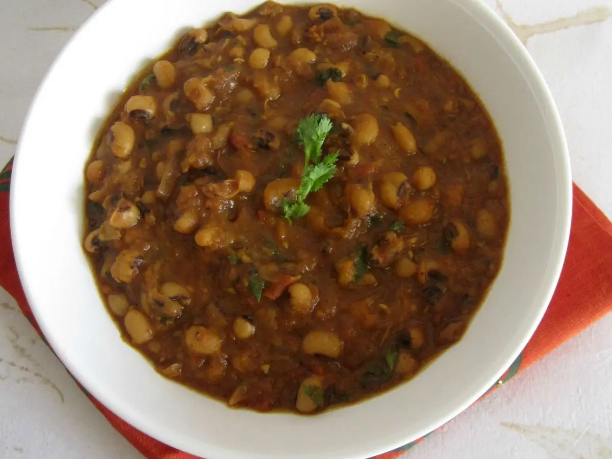 Cuenco blanco de curry de judías carillas con cilantro sobre paño rojo