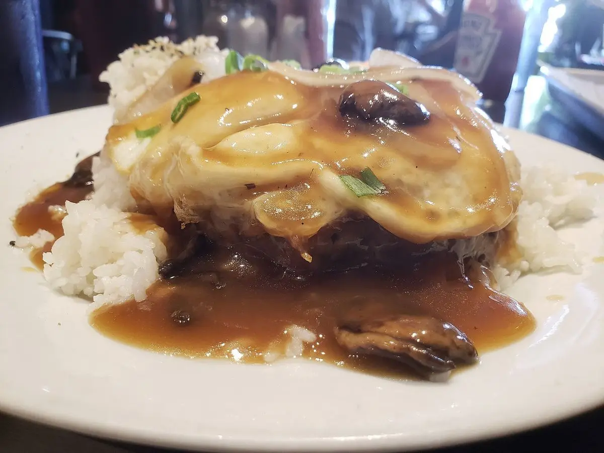 Hamburguesa con salsa de champiñones oscura sobre arroz blanco en un plato, estilo loco moco hawaiano