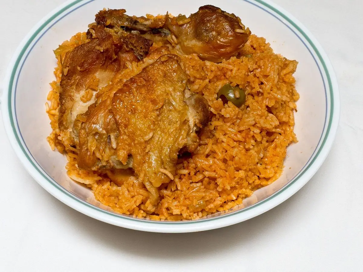 Plato de arroz anaranjado con pollo guisado y aceitunas sobre fondo blanco