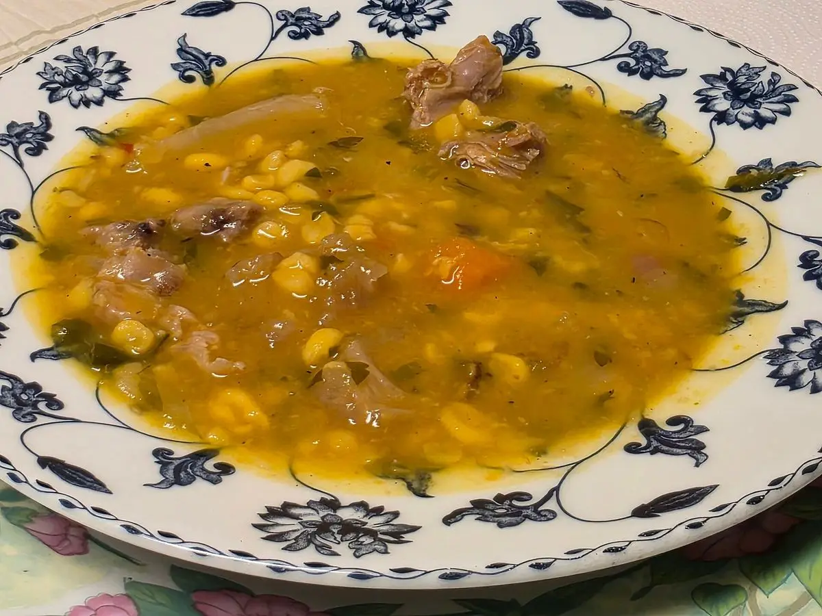Plato hondo azul y blanco con locro de maíz, legumbres, calabaza y trozos de carne