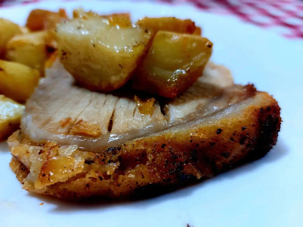 Lonchas gruesas de lomo de cerdo asado con patatas doradas sobre un mantel de cuadros