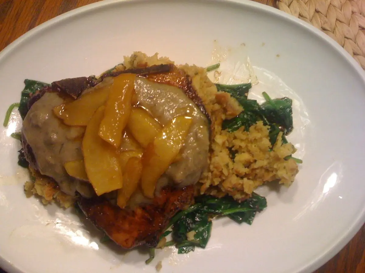 Filete de cerdo cubierto de manzana caramelizada sobre verduras de hoja y arroz en un plato
