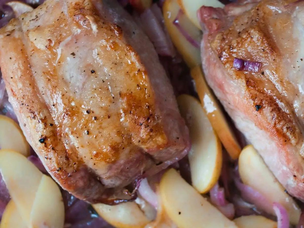 Piezas de lomo de cerdo doradas sobre gajos de manzana y cebolla morada