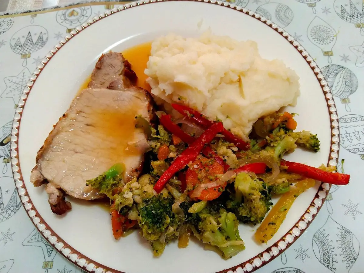 Lomo de cerdo en salsa de naranja con puré de patata y verduras salteadas en un plato