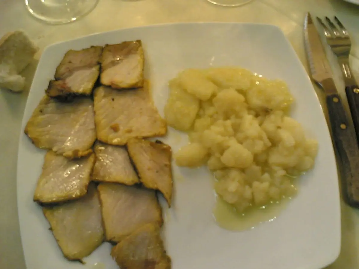 Rodajas de lomo de orza junto a patatas cocidas aliñadas en un plato blanco