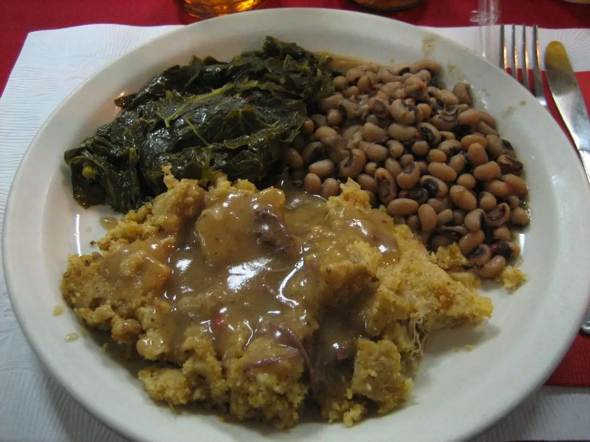 Plato con judías carillas guisadas, verdura de hoja rehogada y una porción de pan de maíz con salsa