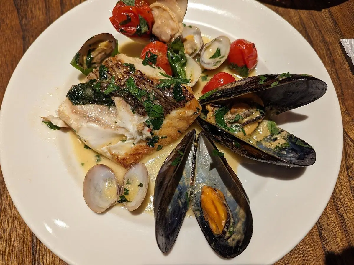 Plato blanco con pescado, mejillones, almejas y tomate en caldo ligero