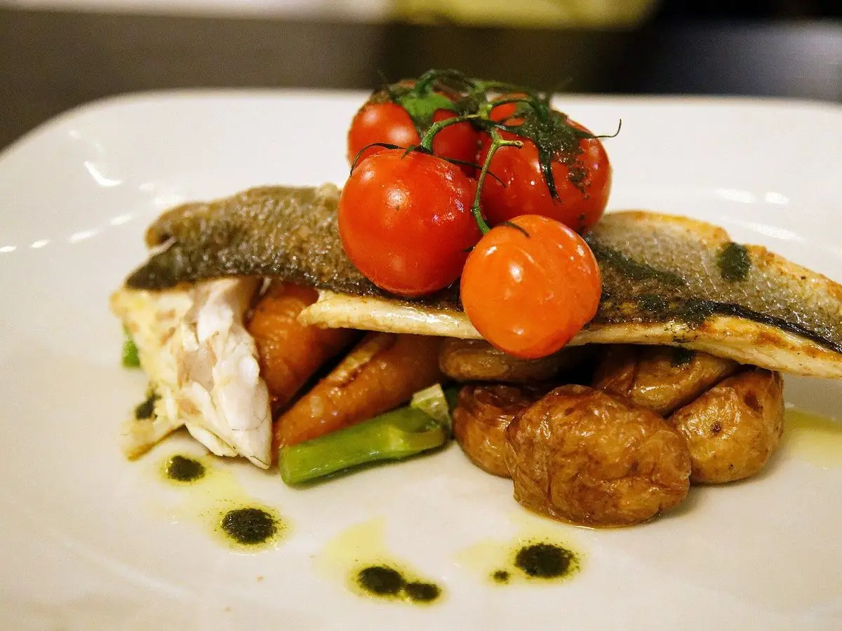 Filete de lubina a la plancha con tomates cherry y patatas pequeñas salteadas en un plato blanco