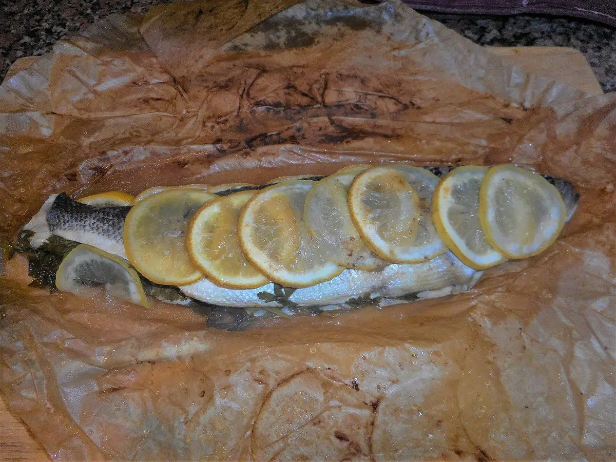Lubina entera cocinada al horno en papel de hornear con rodajas de limón por encima