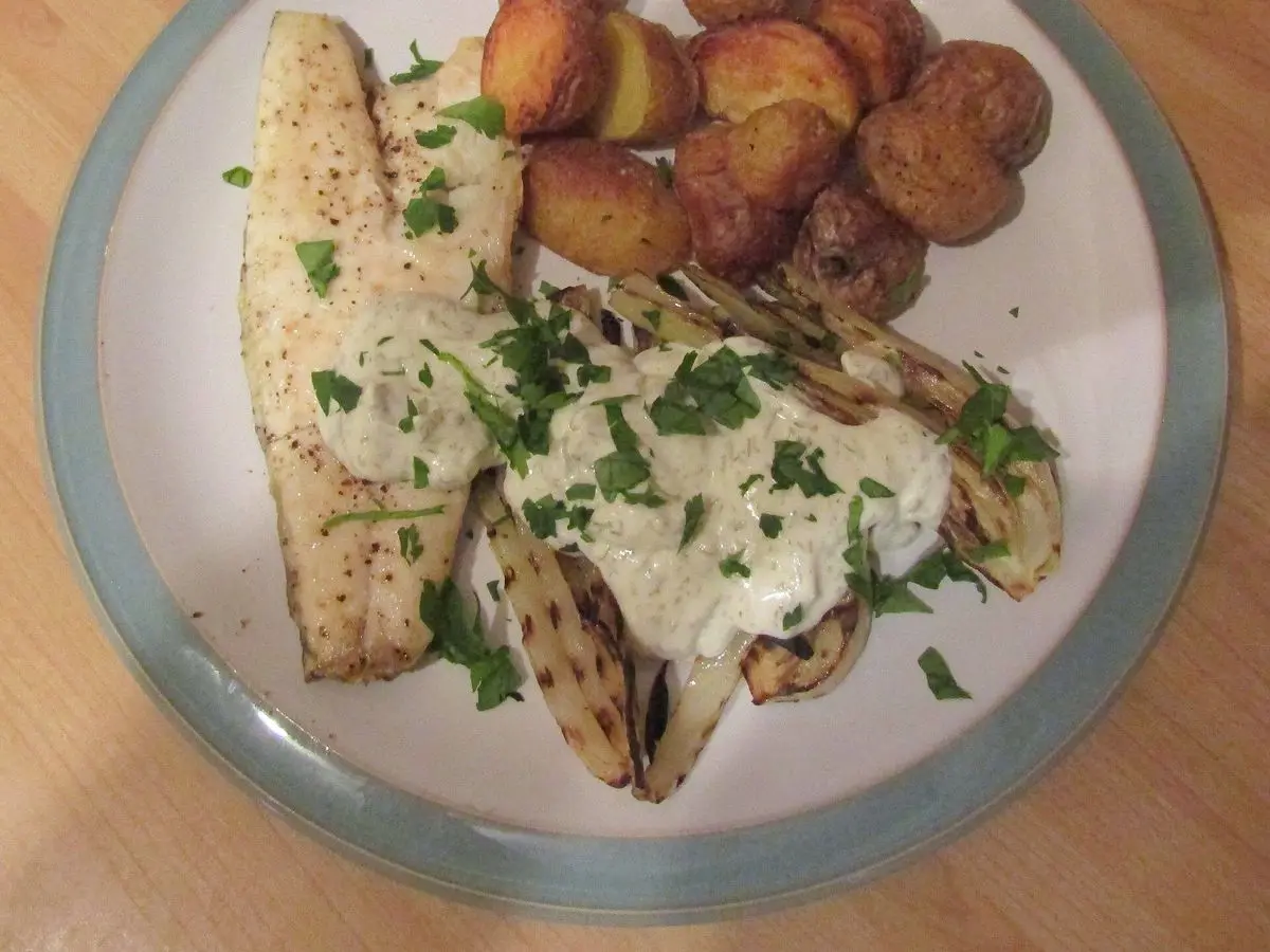 Lubina a la parrilla con patatas nuevas asadas, hinojo a la plancha y hierbas en un plato