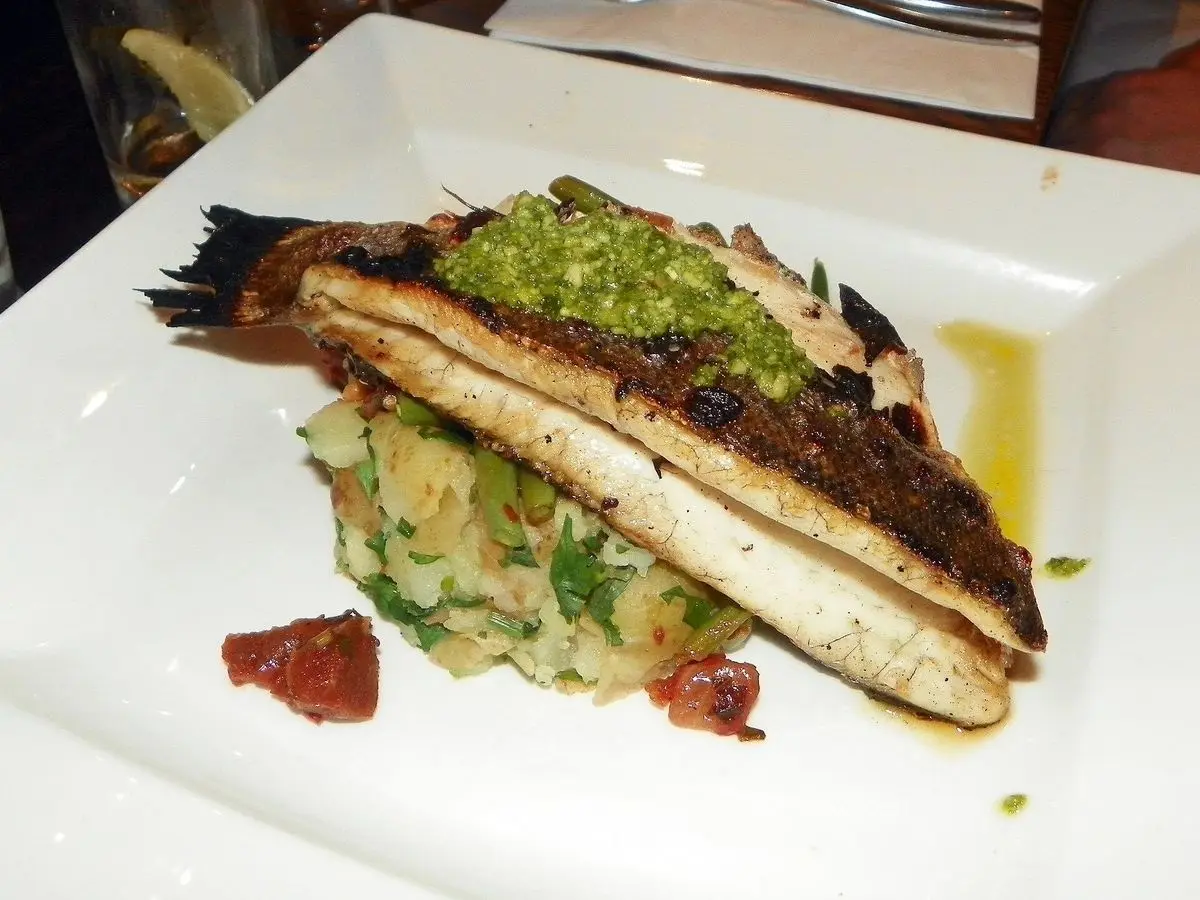 Filete de lubina a la plancha con piel y salsa verde sobre verduras en un plato cuadrado blanco
