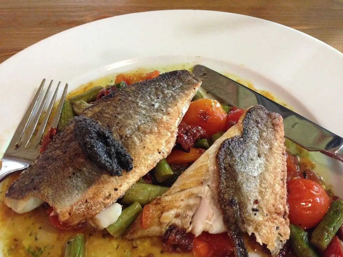 Filetes de lubina con piel dorada sobre verduras y tomate en un plato blanco