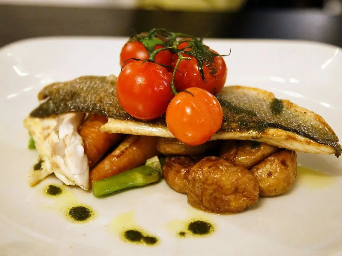 Filete de lubina con la piel dorada sobre patatas asadas, zanahoria y espárrago, con tomates cherry en rama por encima