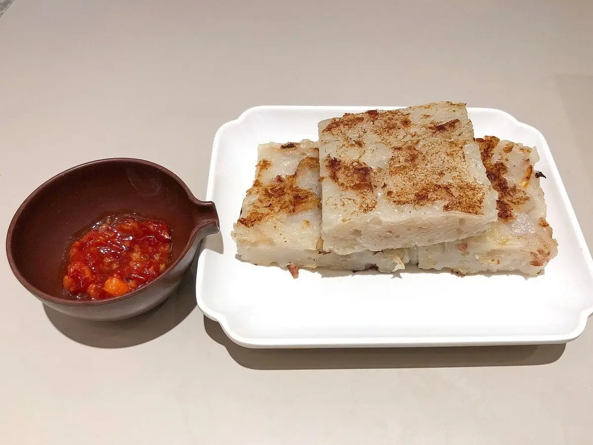 Rectángulos de pastel de nabo daikon dorados a la plancha en un plato blanco con salsa de chile