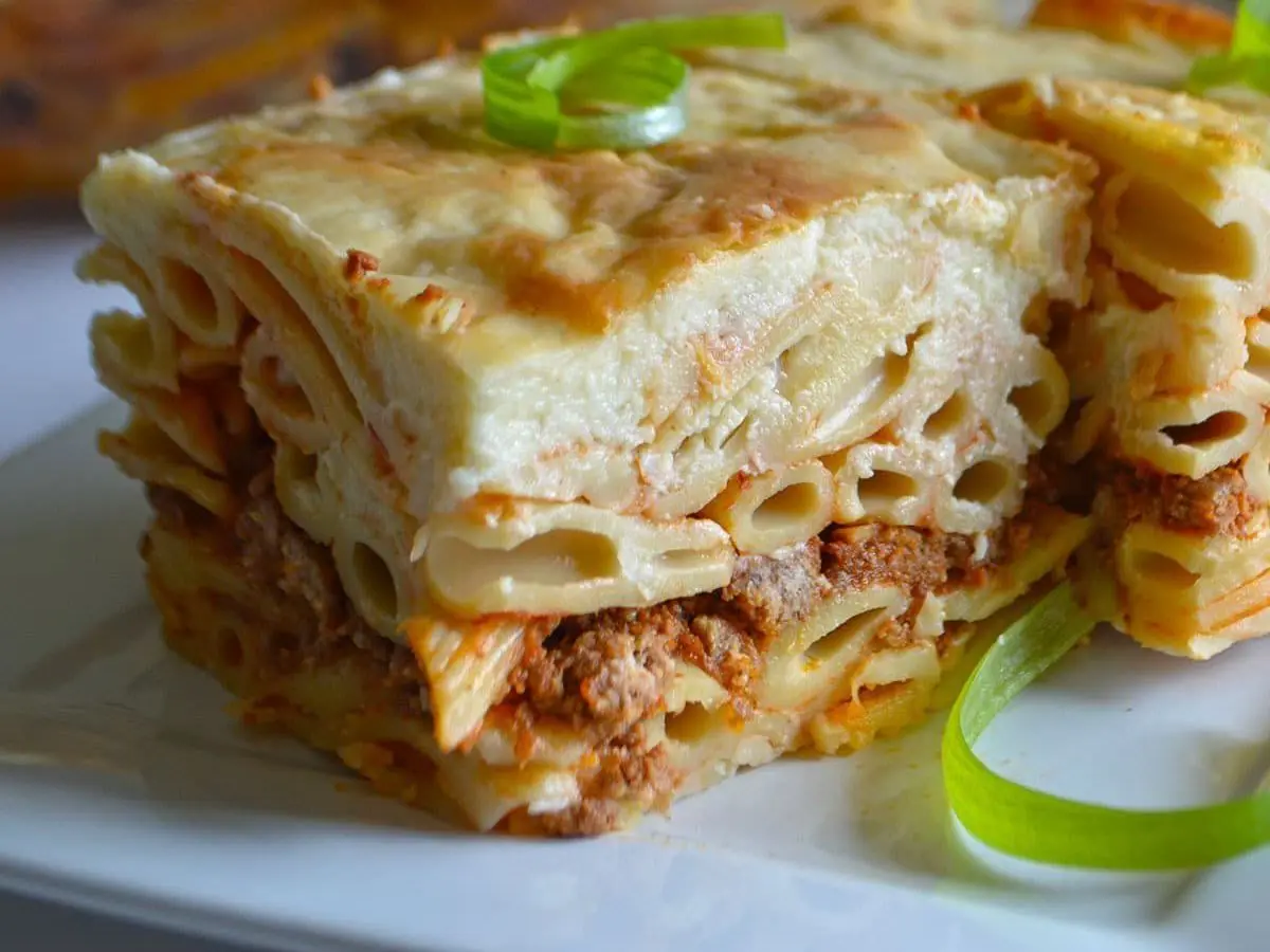 Porción de pastel de macarrones con carne picada y bechamel gratinada con cebolleta por encima