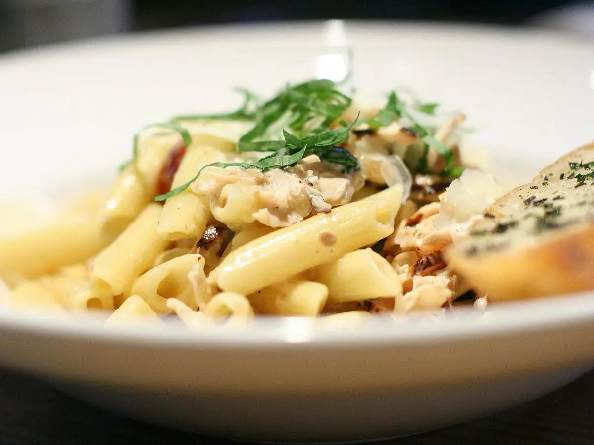 Cuenco de pasta penne con trozos de pollo y albahaca fresca por encima