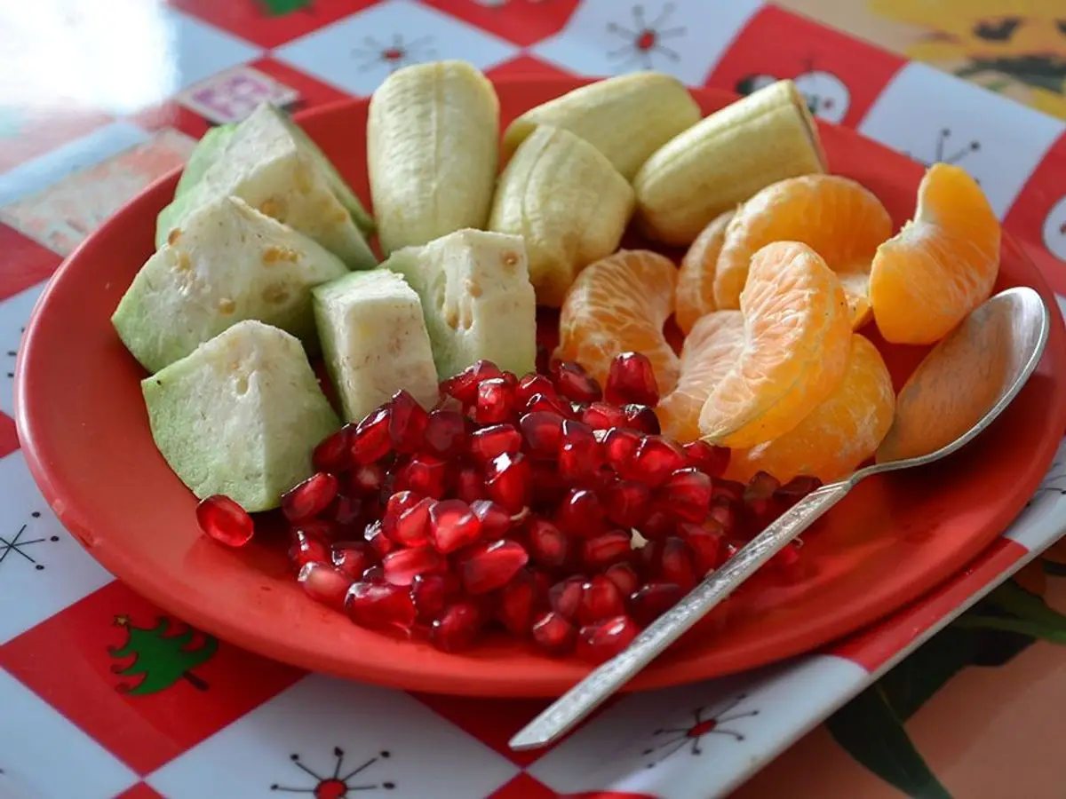 Plato rojo con gajos de mandarina, trozos de fruta pálida y granos de granada