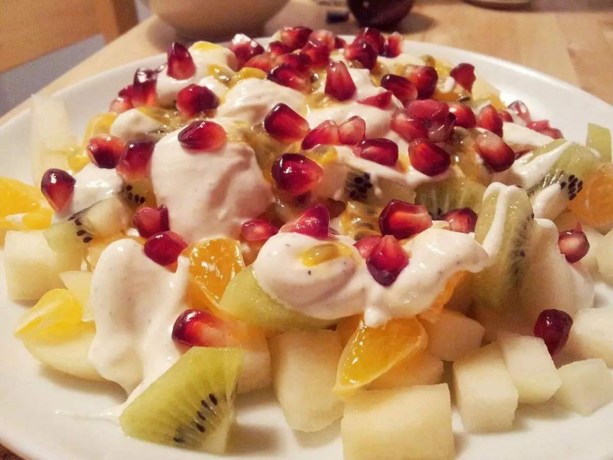 Macedonia de fruta con kiwi, naranja, granada y melón sobre crema blanca en un plato