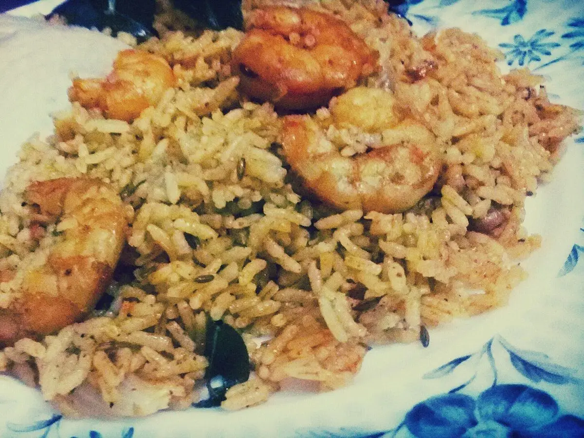 Plato de arroz especiado con gambas grandes encima y una salsa blanca al lado