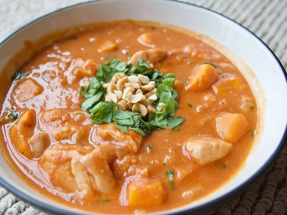 Cuenco de guiso africano de pollo y boniato en salsa naranja de cacahuete con cacahuetes y cilantro por encima