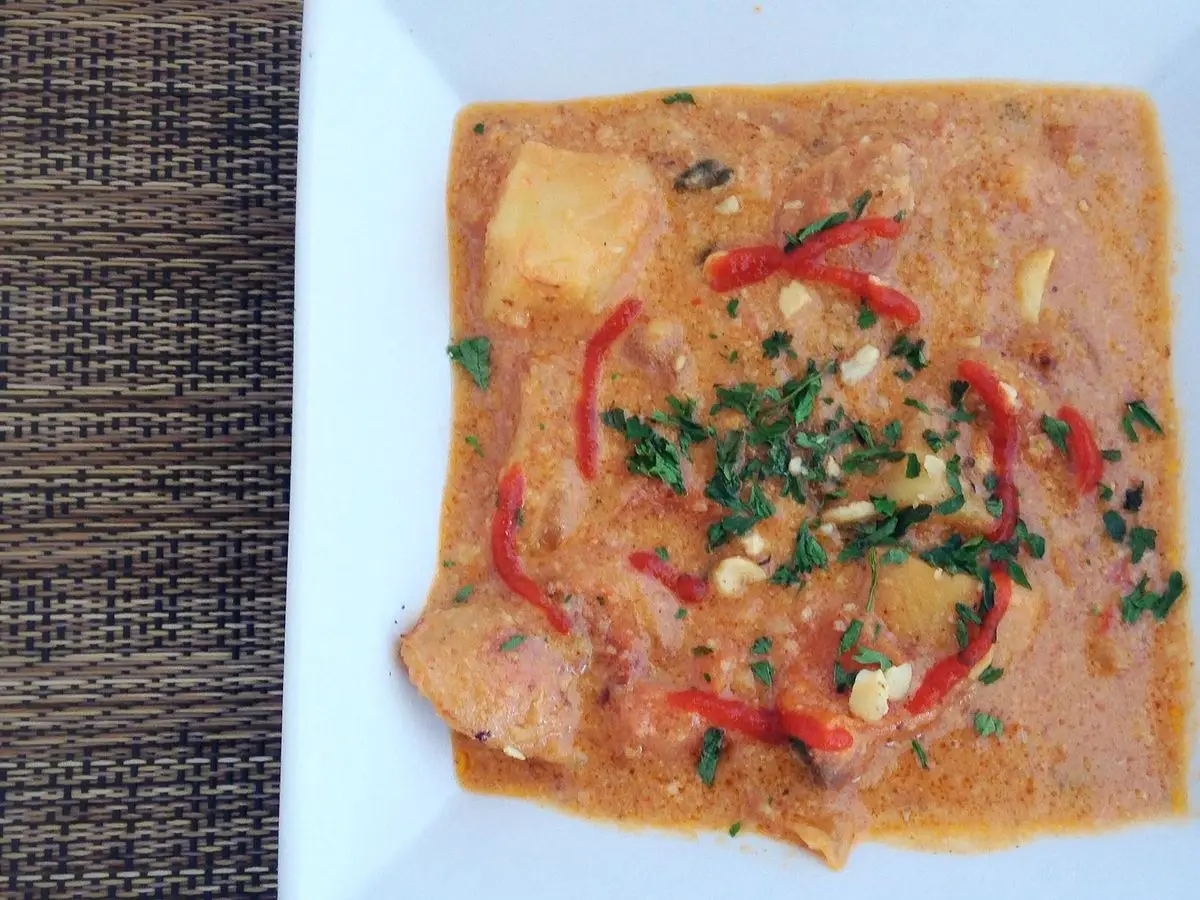 Plato cuadrado de guiso cremoso de cacahuete anaranjado con patata, tiras de pimiento rojo y perejil