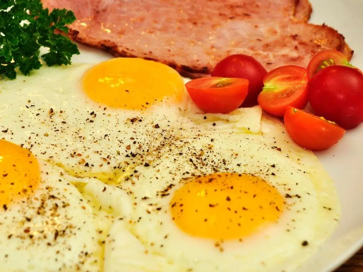 Huevos fritos con lonchas de jamón y tomates cherry en un plato blanco