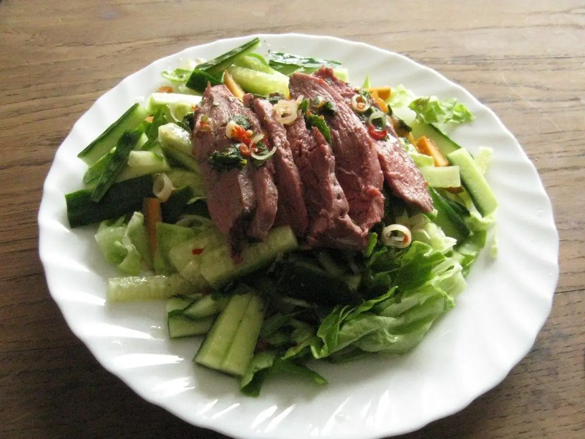 Plato blanco con lonchas de pechuga de pato sobre ensalada de hojas verdes y pepino