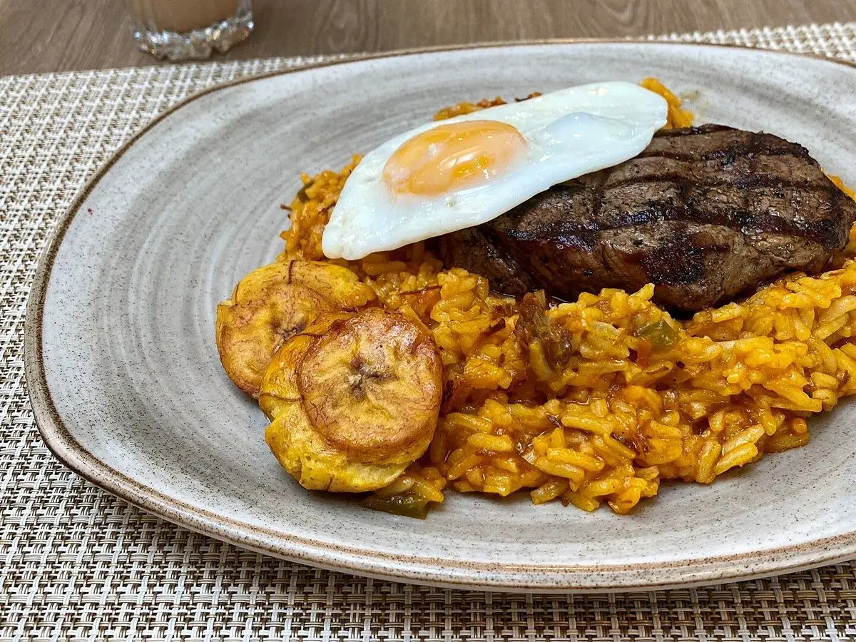 Majadito de arroz con filete de carne, huevo frito y plátano maduro en un plato gris