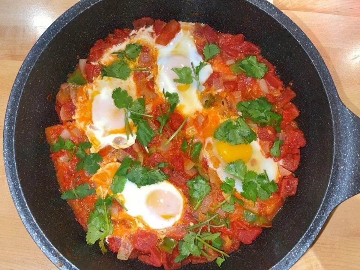 Sartén con huevos cuajados sobre un sofrito de tomate y cebolla, con cilantro fresco por encima