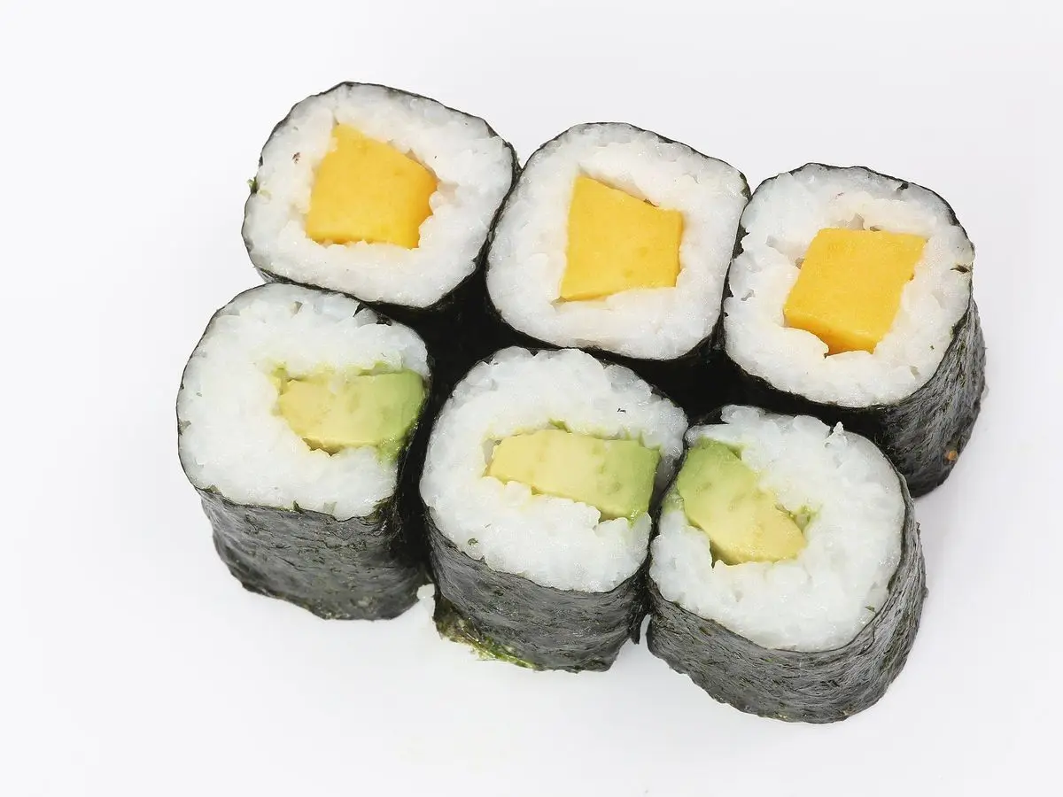 Seis rollitos de maki con alga nori, arroz y relleno de aguacate y de color amarillo sobre fondo blanco