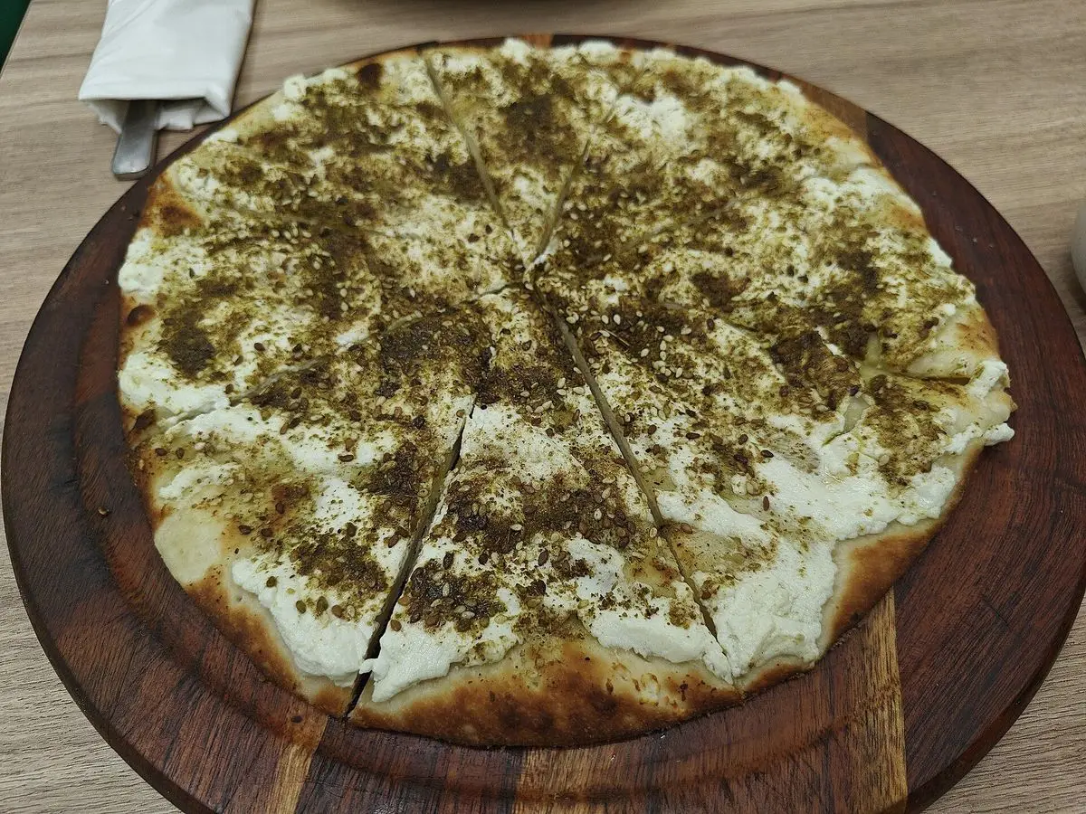 Pan plano redondo cubierto de tomillo y sésamo con base blanca de queso sobre una tabla de madera