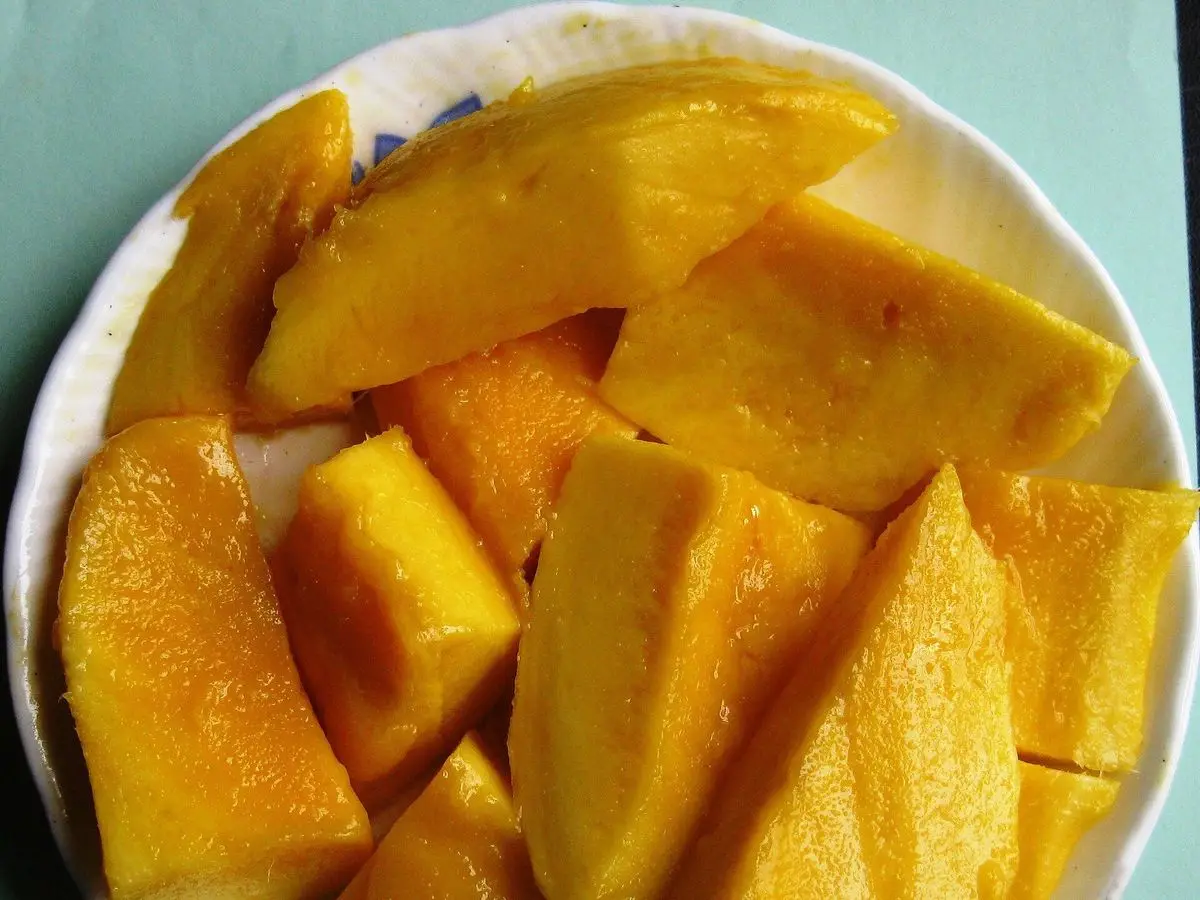 Trozos de mango maduro cortados en cuñas sobre un plato blanco con borde azul