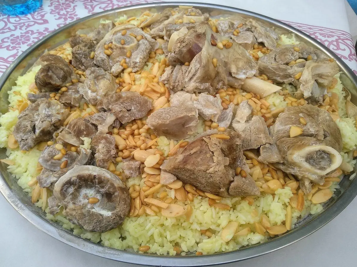 Bandeja grande de arroz amarillo cubierta de trozos de cordero con hueso y frutos secos