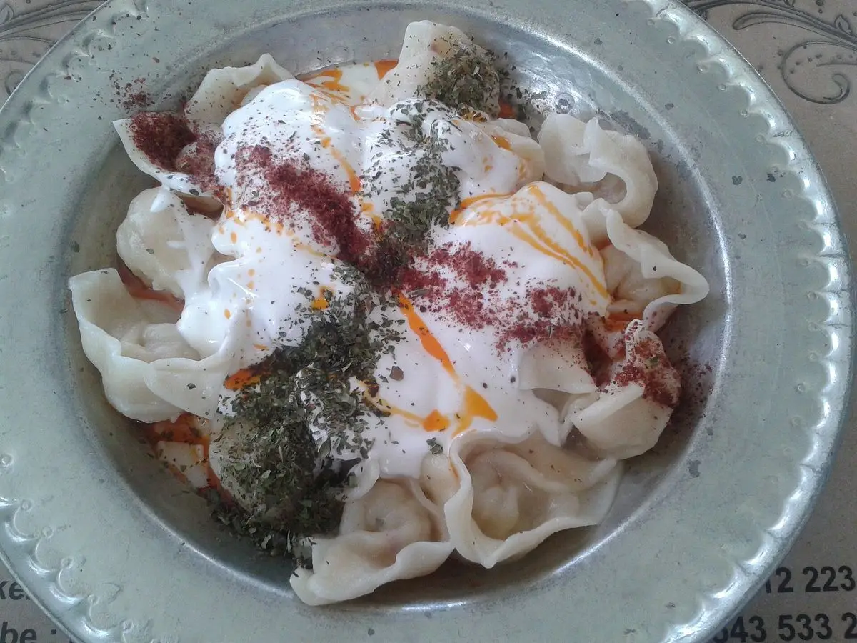 Pequeños manti rellenos cubiertos de yogur con pimentón y eneldo seco en un plato de metal