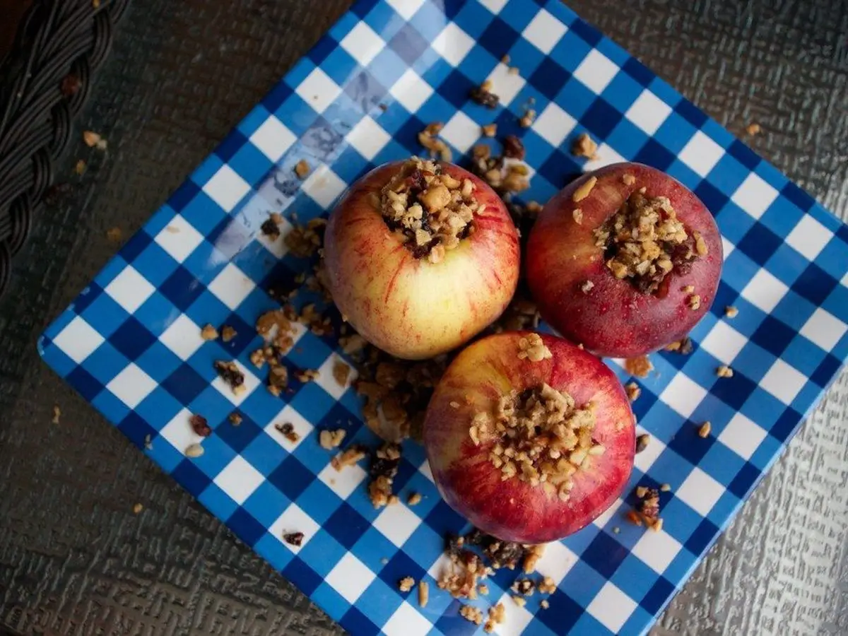 Tres manzanas asadas rellenas con frutos secos y migas sobre un mantel de cuadros azules