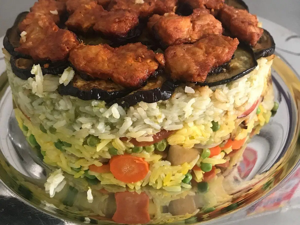 Maqluba desmoldada con capas de arroz, verduras, berenjena y piezas de pollo rebozadas