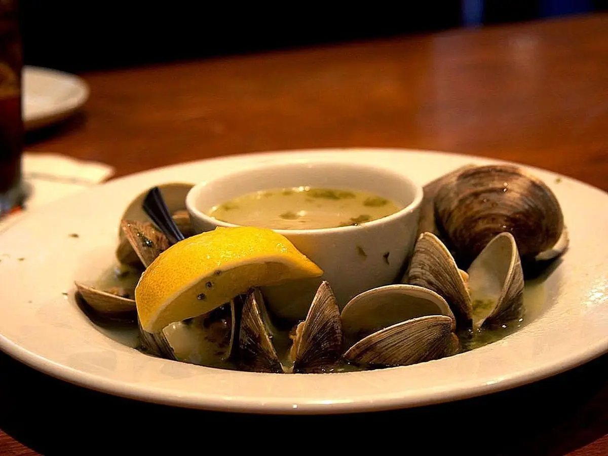 Plato de almejas y mejillones al vapor con una rodaja de limón y un cuenco de caldo