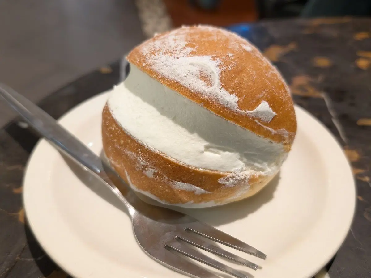 Maritozzo, bollo italiano dulce abierto y relleno de nata montada, sobre un plato blanco con tenedor