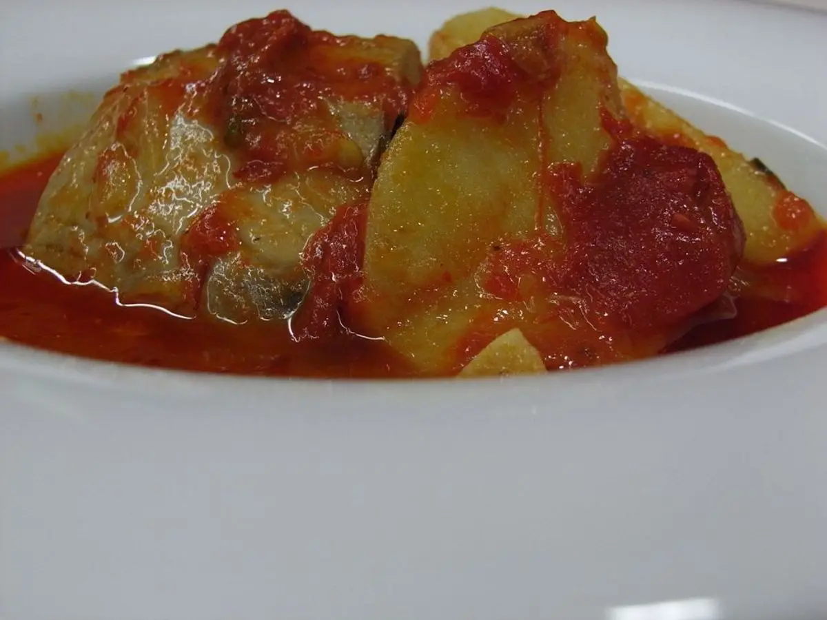 Plato hondo blanco con trozos de pescado y patata en salsa de tomate