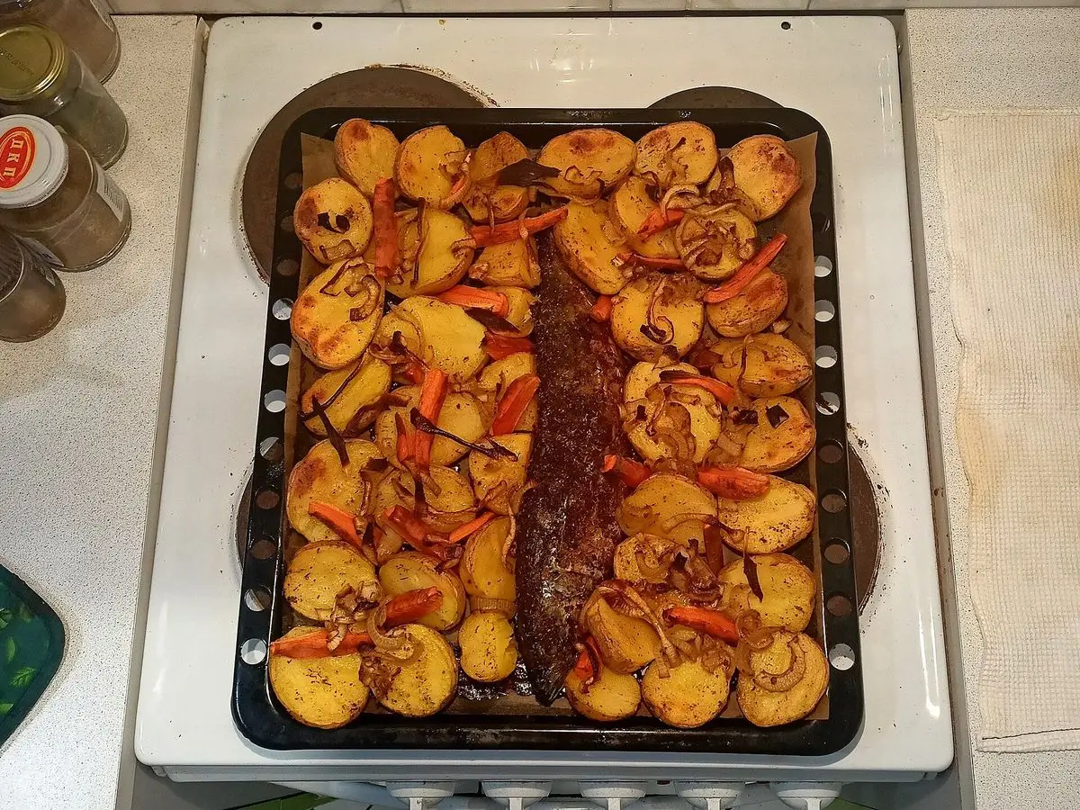 Bandeja de horno con pescado y patatas doradas asadas, vista desde arriba sobre la encimera de la cocina
