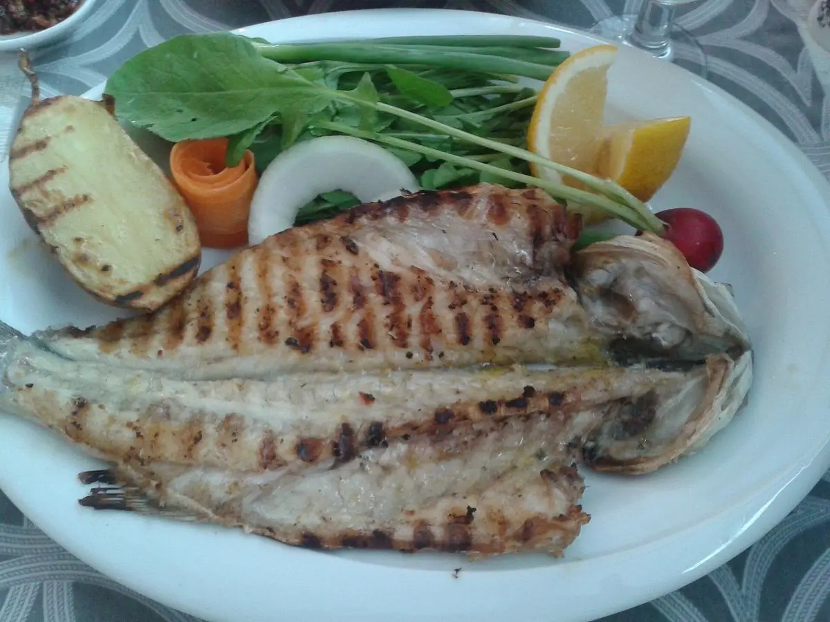 Pescado a la plancha abierto con patata asada, ensalada de hojas verdes, tomate y rodajas de limón en un plato